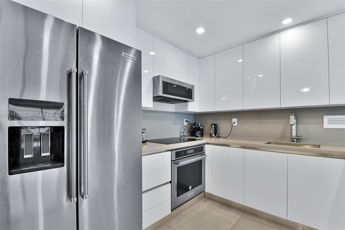 Kitchen featuring high-gloss white cabinetry, solid surface countertops, recessed lighting, and stainless steel appliances including a built-in oven, 