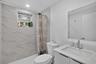 Bathroom featuring large-format stone-finish wall tiling, white vanity with a speckled countertop, integrated sink, chrome faucet, and a frameless mir