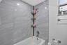 Bathtub surround featuring large-format gray veined tile, integrated metallic shower head, and wall-mounted metal towel rack