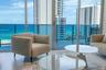 Floor-to-ceiling glass sliding doors, private balcony with glass railing, large-format tile flooring, and coastal backdrop