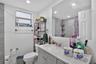 Bathroom featuring gray shaker-style vanity cabinetry, solid-surface countertop with integrated basin, polished chrome faucet, large-format wall tilin