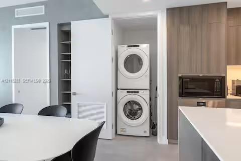 Built-in laundry closet with stacked washer and dryer, adjacent custom shelving, and modern cabinetry featuring a built-in microwave