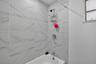 Full-height shower enclosure featuring large-format stone-patterned wall tile, chrome plumbing fixtures, and a white soaking tub