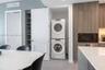 Built-in laundry closet with stacked washer and dryer, adjacent custom shelving, and modern cabinetry featuring a built-in microwave