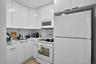 Kitchen featuring high-gloss white cabinetry, solid-surface countertops, stainless steel sink with high-arc faucet, and white appliances including a b