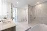 Dual-sink vanity with light-toned countertop, freestanding soaking tub, glass-enclosed walk-in shower with tiled surround, and separate enclosed water