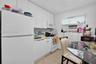 Kitchen featuring white flat-panel cabinetry, full-size white refrigerator, integrated microwave, and textured stone-finish flooring