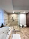 Full-size jetted soaking tub, walk-in shower with stone-tile surround, built-in shower bench, and stone-tile flooring