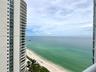 High-rise balconies with glass railings overlooking a coastal shoreline and ocean expanse