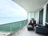 Curved private balcony featuring stone flooring, a glass-panel railing, and floor-to-ceiling glass sliding doors
