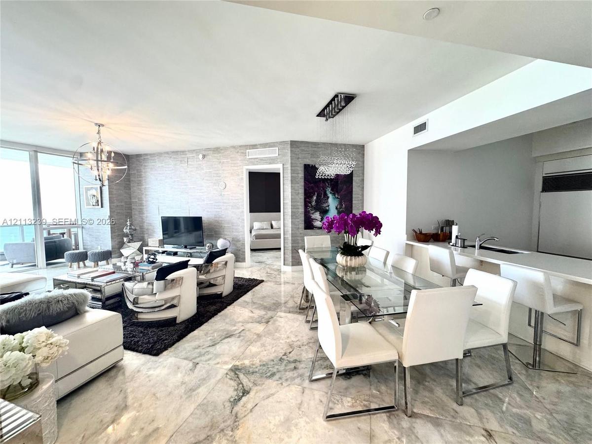 Open-concept living space featuring large-format polished stone flooring, textured wall coverings, floor-to-ceiling windows, and a breakfast bar with 