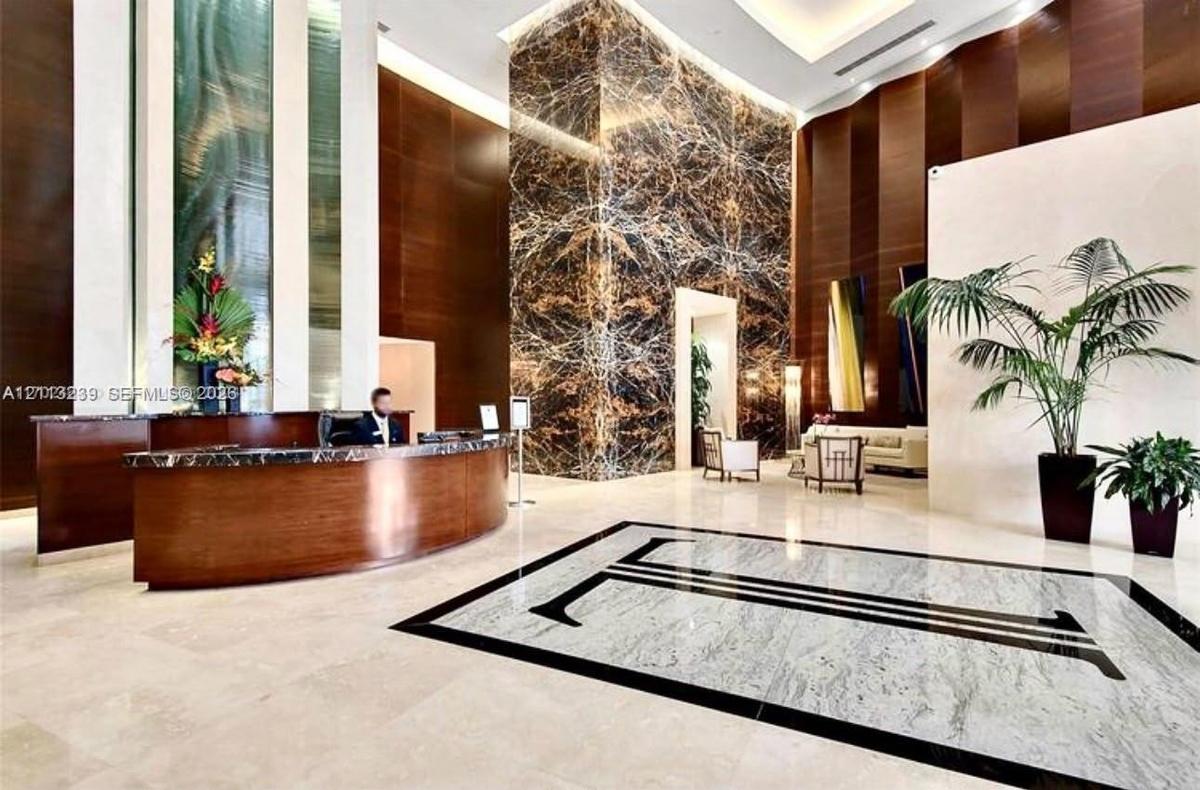 Grand lobby entrance featuring high-contrast stone flooring, a prominent full-height natural stone feature pillar, recessed cove lighting, and curved 