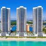 High-rise residential towers featuring glass-paneled balconies, exterior swimming pools, direct beachfront access, and water-front placement