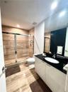 Bathroom featuring high-gloss cabinetry, black stone countertop with an integrated basin, large-format neutral-toned stone tile flooring, and a walk-i