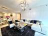 Open-concept living space featuring high-gloss, full-height wall paneling, polished stone flooring, a multi-arm spherical chandelier, and a linear cry