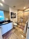 Full-height vanity mirror, dark stone-surface countertop, white cabinetry, walk-in shower with stone tile surround, and large-format stone floor tile