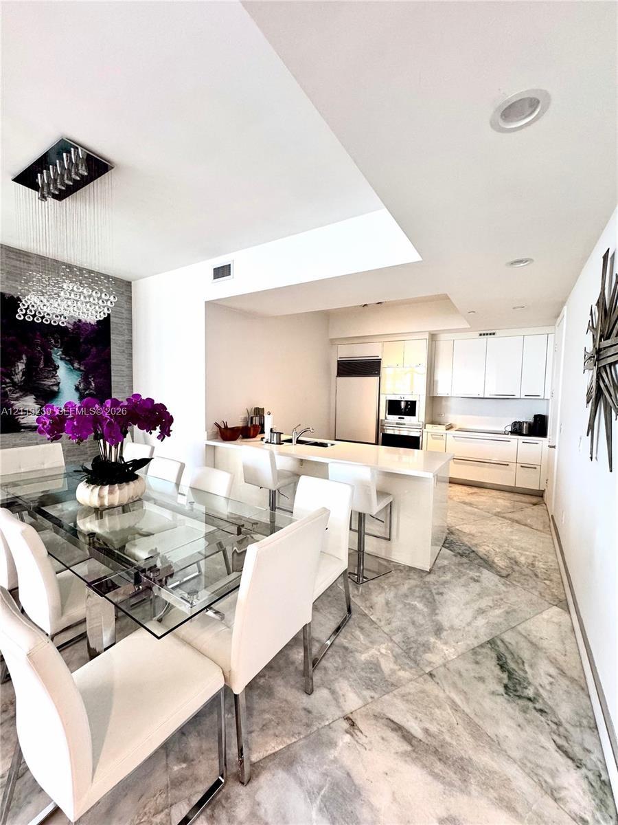 Kitchen featuring white cabinetry, solid-surface countertops, built-in appliances, and light-toned stone-finish flooring with geometric tile patterns