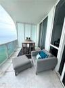 Covered balcony featuring large-format stone tile flooring, a glass panel railing, and expansive floor-to-ceiling glass sliding doors