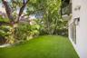 Private backyard featuring synthetic turf, mature trees, wood privacy fencing, a second-story balcony with metal railings, and exterior wall-mounted l