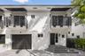 Two-story stucco exterior featuring horizontal black metal balcony railings, a multi-paneled garage door, geometric entry steps, and matching black me