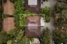 Aerial perspective of a multi-sectioned hip roof featuring dark shingle tiling, integrated solar panels, and surrounding mature landscaping