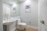 Pedestal sink with high-arc polished chrome faucet, expansive wall-mounted mirror, one-piece dual-flush toilet, and wood-finish flooring