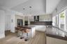 Kitchen featuring wood-finish cabinetry, stone countertops, stainless steel appliances, double wall ovens, and dual pendant lighting