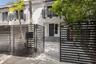 Exterior facade featuring a paved stone driveway, horizontal slat metal privacy fencing, solid panel entry door, and upper-level balconies with matchi