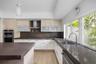 Kitchen featuring light wood-finish cabinetry, solid-surface countertops, a stainless steel chimney-style range hood, built-in double ovens, and a dua