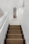Staircase featuring dark-finished wooden treads, textured stair runner with a bordered edge, white wall-mounted handrail, and high-reaching walls with