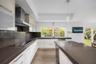 Modern kitchen featuring white flat-panel cabinetry, dark stone-finish countertops, stainless steel range hood, built-in cooktop, and wood-finish floo