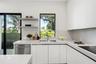 Minimalist kitchen featuring matte white flat-panel cabinetry, light-toned stone-surface countertops, stainless steel undermount sink, built-in dishwa