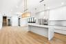 Modern kitchen featuring flat-panel cabinetry, a waterfall-edge quartz island, stainless steel built-in appliances, decorative pendant lighting, and w