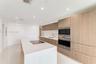 Kitchen featuring wood-finish cabinetry, a white countertop island with an integrated cooktop, stainless steel wall-mounted oven and microwave, stone 