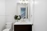 Bathroom featuring a dark wood-finish vanity, white countertop with an integrated basin, wall-mounted rectangular mirror, three-light fixture with cyl