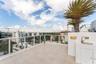 Rooftop terrace featuring light-toned tile flooring, a white glass-paneled railing, integrated wet bar with a stainless steel sink, and mature palm tr