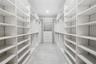 Walk-in closet featuring extensive built-in white shelving, integrated clothing rods, a central drawer bank, and tile flooring