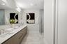 Dual-sink floating vanity with neutral cabinetry, expansive wall-mounted mirror, light-toned stone-finish flooring, and glass-enclosed shower with ful