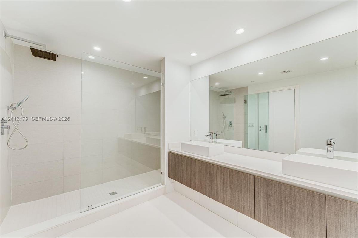 Dual vanity featuring rectangular vessel sinks, quartz countertops, wood-finish cabinetry, frameless glass shower enclosure, and ceiling-mounted rainf