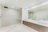 Dual vanity featuring rectangular vessel sinks, quartz countertops, wood-finish cabinetry, frameless glass shower enclosure, and ceiling-mounted rainf