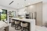 Contemporary kitchen featuring floor-to-ceiling flat-panel cabinetry, a waterfall-edge stone island, built-in stainless steel appliances, and dual pen