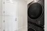 Stacked washer and dryer unit with a sleek black finish, paired with a white Shaker-style door featuring polished chrome hardware and large-format til