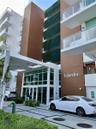 Modern building facade featuring wood-finish paneling, vertical green wall detailing, expansive floor-to-ceiling glass entryway, white structural acce