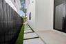 Side exterior featuring white stucco siding, a concrete paver walkway set in artificial turf, a black metal corrugated privacy fence, and a glass-pane