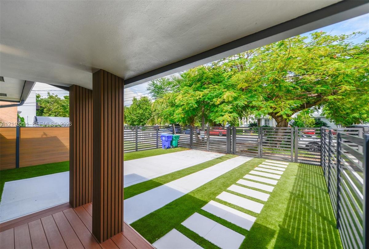 Covered patio featuring wood-finish decking and vertical slat columns, accompanied by a landscaped area with synthetic turf, concrete pavers, and hori