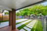 Covered patio featuring wood-finish decking and vertical slat columns, accompanied by a landscaped area with synthetic turf, concrete pavers, and hori