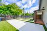 Fenced exterior space featuring concrete paving, synthetic turf, wood-finish decking, and slat-style metal fencing