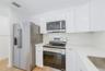 Kitchen featuring white high-gloss cabinetry, stone-finish countertops, stainless steel appliances, and wood-finish flooring