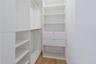 Built-in white storage system featuring adjustable shelving, integrated hanging rods, and dual drawers with silver-tone hardware over wood-finish floo