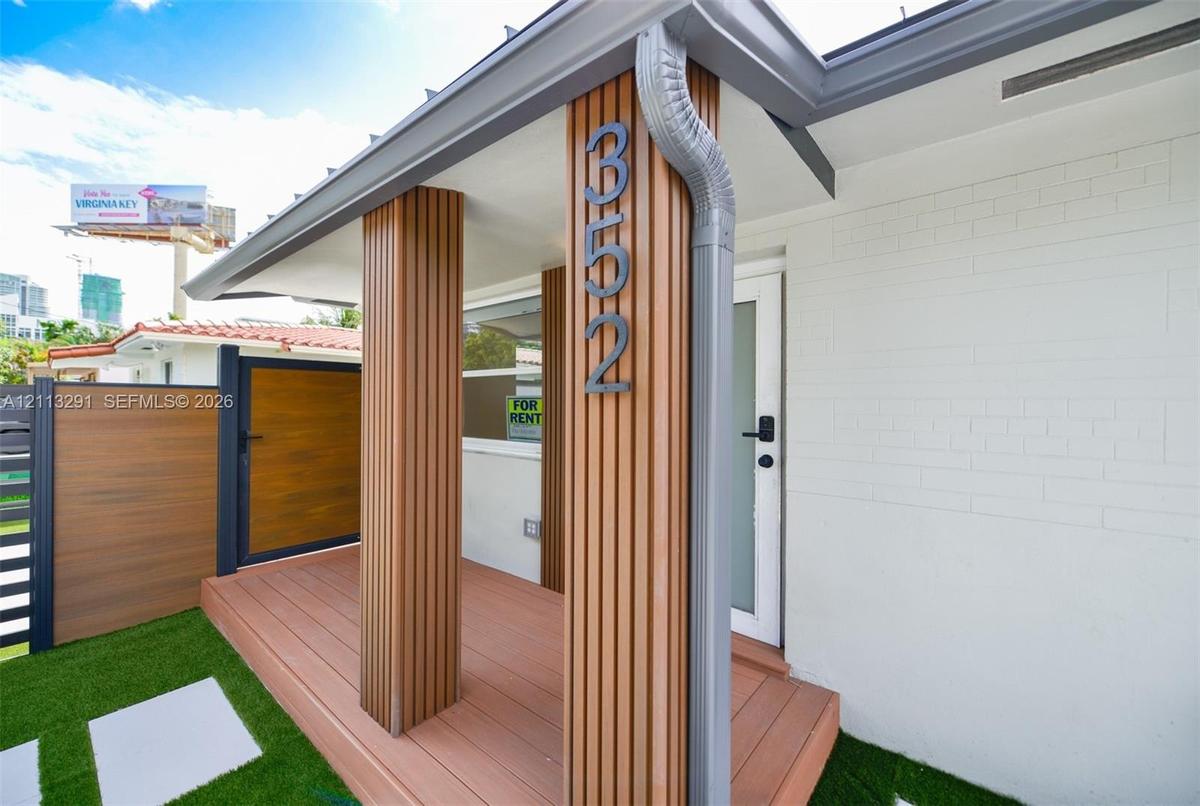 Entrance featuring a composite deck, vertical wood-slat accent columns, white painted brick exterior, and a privacy fence with a matching wood-finish 